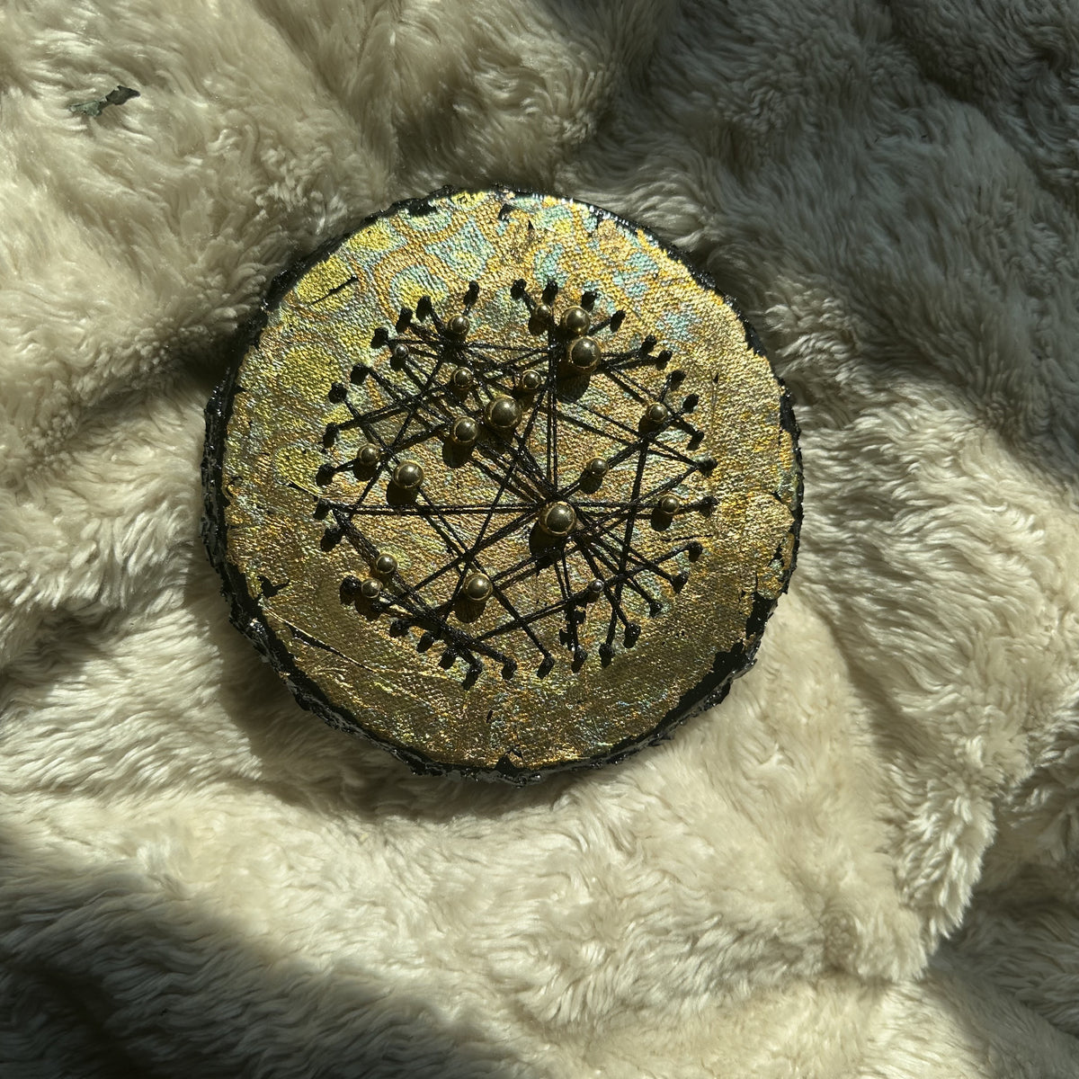 Rundt mixed media-kunstverk, 15 cm diameter, med gyllent skimrende overflate og sorte tråder med perler i konstellasjonsmønster. Constellations III av Art by Emerense