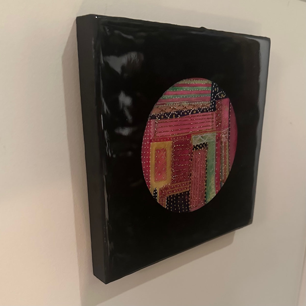 Kvadratisk kunstverk, 20×20 cm, sett fra siden. Blank sort epoxyfinish viser dybden. Fargerikt rundt motiv i rosa, rød og gull med teksturlignende detaljer. Fargesymfoni av Art by Emerense
