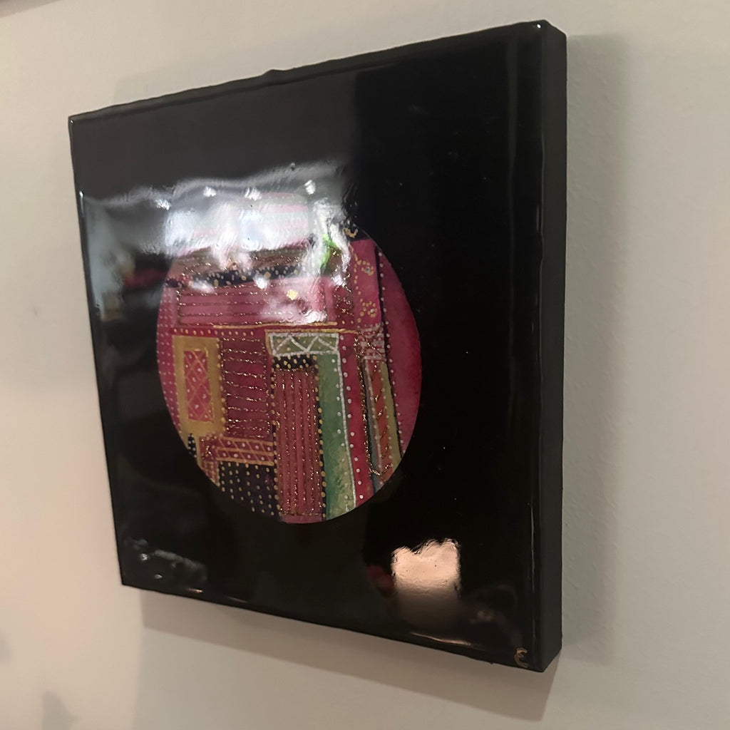 Kvadratisk kunstverk, 20×20 cm, sett fra høyre side. Sort blank epoxy reflekterer lyset. Rund fargerik sirkel i rosa, grønt og gull synlig. Fargesymfoni av Art by Emerense
