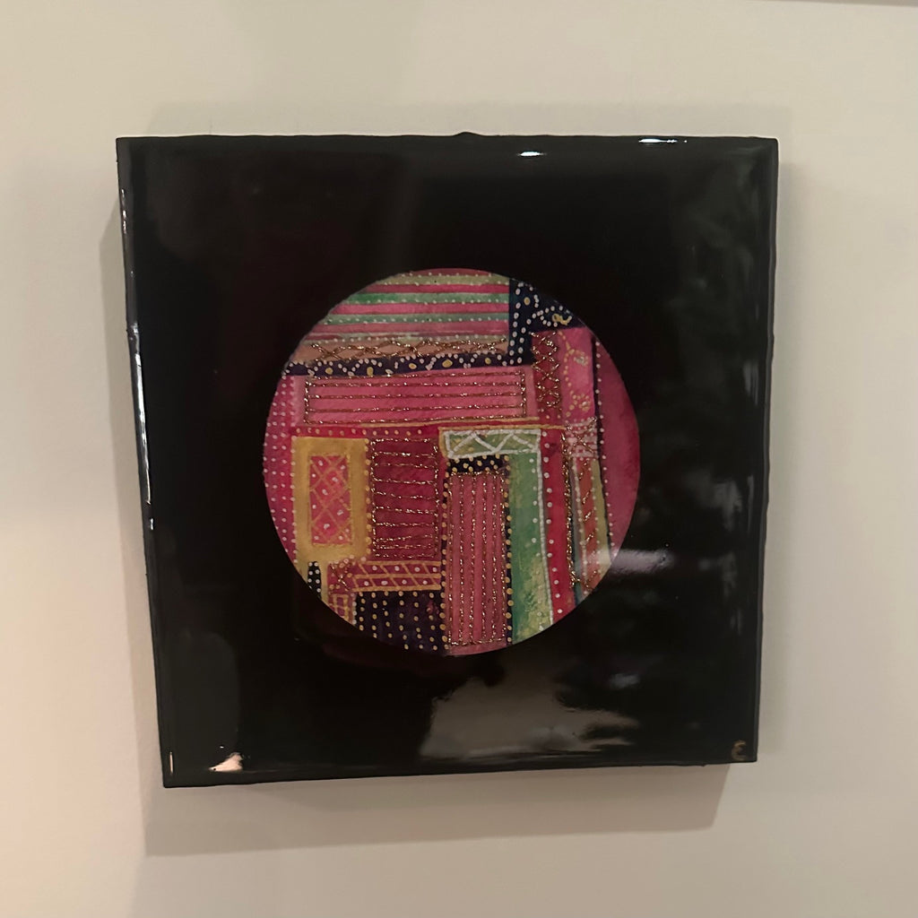 Kvadratisk kunstverk, 20×20 cm, med speilblank sort epoxyoverflate. Rund sirkel i midten med fargerikt tekstilinspirert mønster i rosa, rød, gull, grønn og sort. Fargesymfoni, epoxy og mixed media. Art by Emerense
