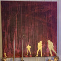 Stort kvadratisk kunstverk, 100×100 cm, med fire gyllne siluetter mot dyp sort og rød bakgrunn med rosa og røde dryppende striper. Én figur i ferd med å gå bort fra de andre. Gjengangere, akryl og mix medium. Art by Emerense