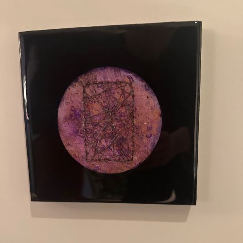 Kvadratisk kunstverk, 20×20 cm, hengt på beige vegg. Speilblank sort epoxyoverflate med rund lilla og kobberfarget sirkel i midten. Intrikat mørkt trådenett i rektangulær form over sirkelen. Kosmisk vev, epoxy og mixed media. Art by Emerense