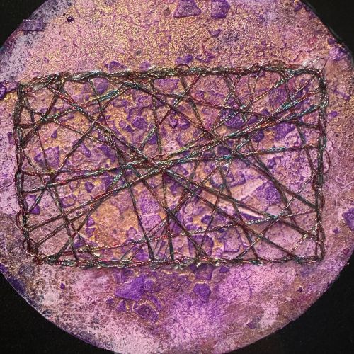 Nærbilde av rund sirkel, ca. 15 cm diameter, med lilla, rosa og kobber teksturert overflate. Intrikat mørkt metallisk trådenett i rektangulær form flettet over overflaten. Detalj fra Kosmisk vev av Art by Emerense
