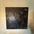 Stort kvadratisk kunstverk, 100×100 cm, hengt på hvit vegg. Mørk sort og dyp blåsvart strukturert overflate med sølvglitter og små lyspunkter som stjerner. Rød lys akkord øverst til høyre. The Big Bang, mixed media på lerret. Art by Emerense
