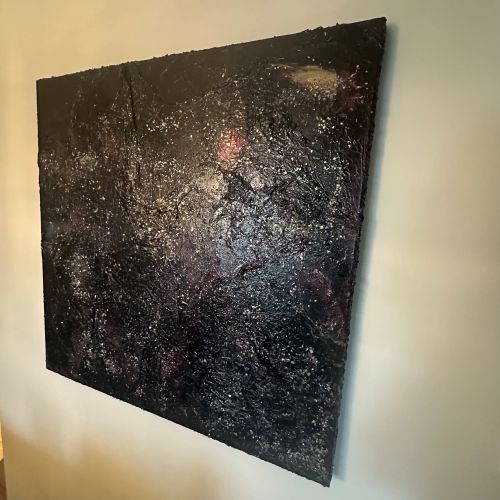 tort kvadratisk kunstverk, 100×100 cm, sett fra siden på hvit vegg. Tykk grov sort struktur med glitrende sølvpartikler og rødt lyspunkt synlig. The Big Bang av Art by Emerense