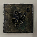Kvadratisk kunstverk 20×20 cm med sorte tredimensjonale halvkuler med gullkanter på mørk bronsefarget teksturert lerret. Adore Sort av Art by Emerense