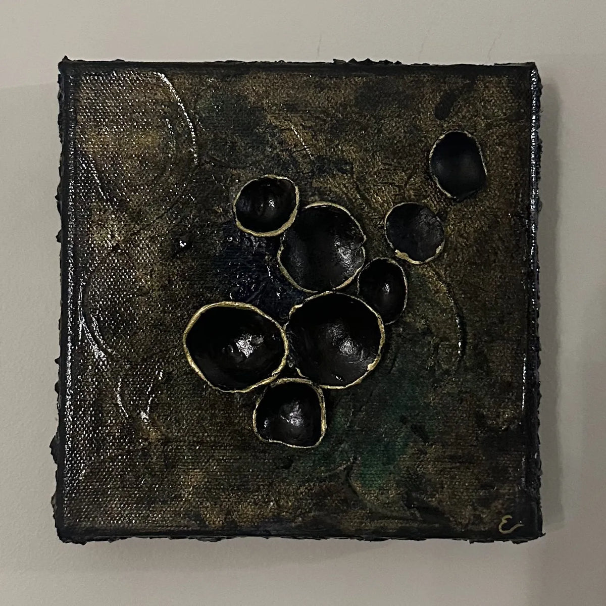 Kvadratisk kunstverk 20×20 cm med sorte tredimensjonale halvkuler med gullkanter på mørk bronsefarget teksturert lerret. Adore Sort av Art by Emerense