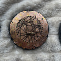 Rundt mixed media-kunstverk, 15 cm diameter, med varm kobber og gullfarget iriserende overflate. Sorte tråder og bronseperler i stjernemønster. Constellations II av Art by Emerense