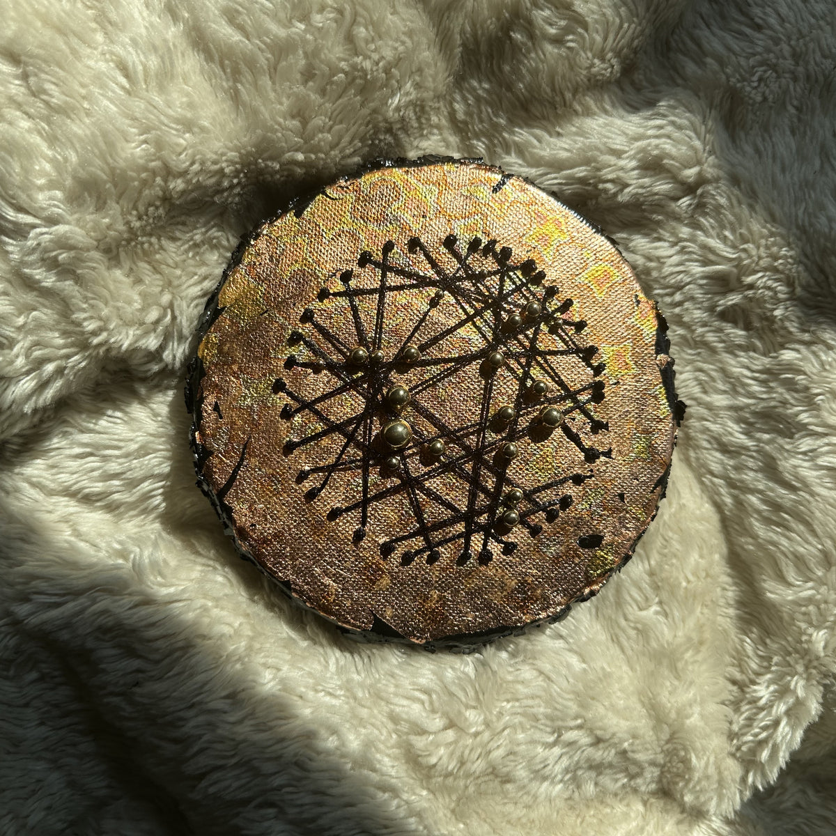 Rundt mixed media-kunstverk, 15 cm diameter, kobber og gull med sorte tråder og metallperler. Fotografert i naturlig lys på hvit fluffy overflate. Constellations II av Art by Emerense
