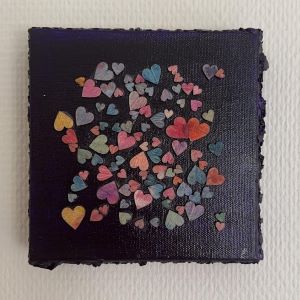 Kvadratisk kunstverk, 20×20 cm, med fargerike små hjerter i rosa, lilla, gult og hvitt på sort lerret. Hjerter i fleng, mixmedia. Art by Emerense