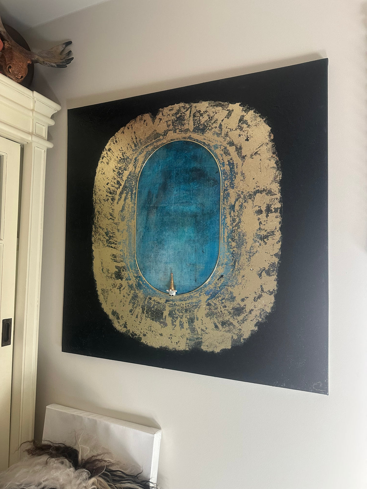 Stort kunstverk, 80×80 cm, hengt over hvitt møbel på hvit vegg. Blå oval portal med gullramme og tekstur på sort lerret. Jeg viser deg universet av Art by Emerense