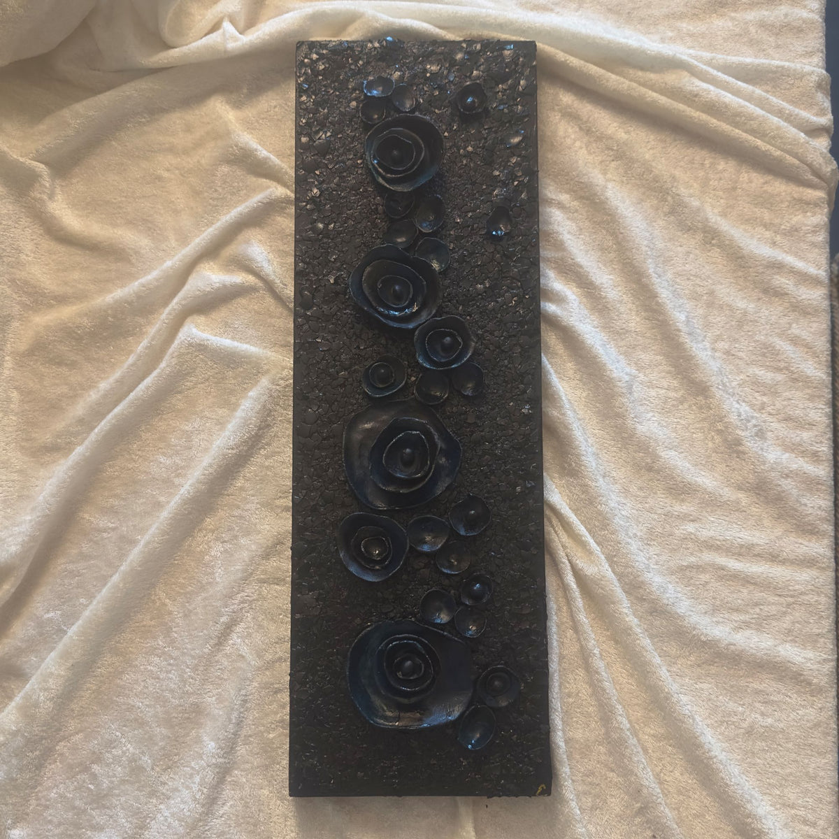 Smalt skulpturelt maleri med mørke tredimensjonale roser på sort teksturert lerret. 40×15 cm, mix medium. Art by Emerense