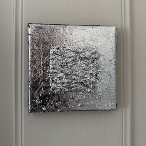 Kvadratisk kunstverk med lysreflekterende sølvfolie og fin tekstur på sort kant. 20×20 cm, mix media. Art by Emerense
